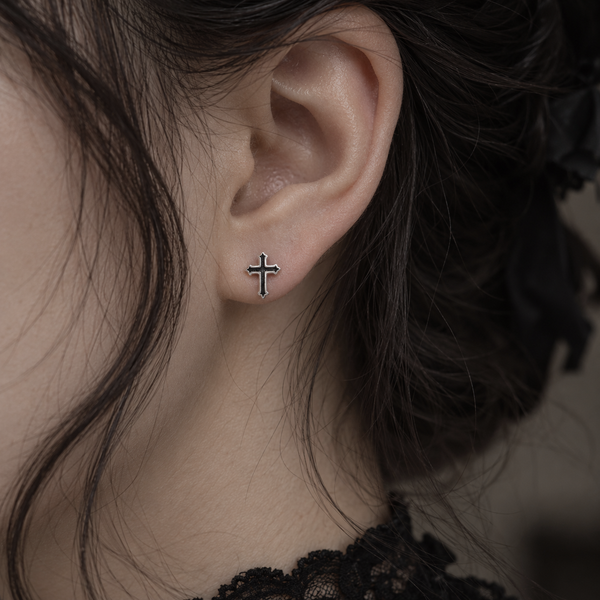 A close-up of a person's ear wearing a small silver cross stud earring.