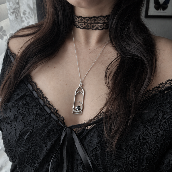 A close-up lifestyle shot of a woman wearing a gothic-style silver pendant necklace with a black cat silhouette and a small black cat eye, styled with a black lace choker and a black lace top.