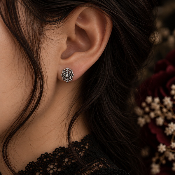 A close-up of a person's ear wearing a small geometric star-shaped stud earring with silver-toned metal and dark inlay details, against a dark background with blurred flowers.