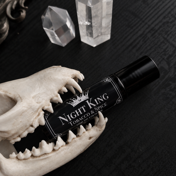 A black cylindrical rollerball bottle labeled 'Night King Tobacco & Spice' with white lettering, displayed in the jaw of an animal skull