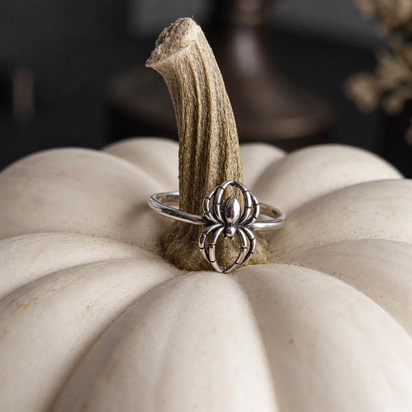 A silver spider ring with a detailed spider head on a band, displayed on the stem of a white decorative pumpkin.