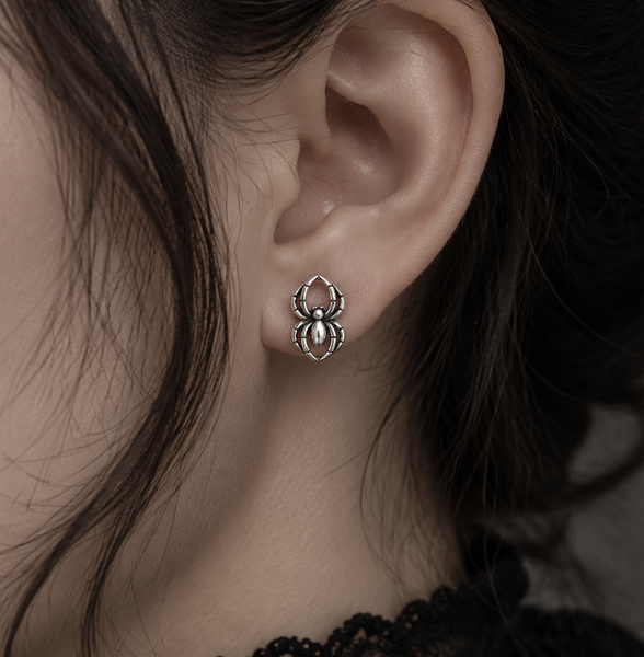 A close-up of a person's ear wearing a small spider-shaped stud earring in polished silver-tone metal.